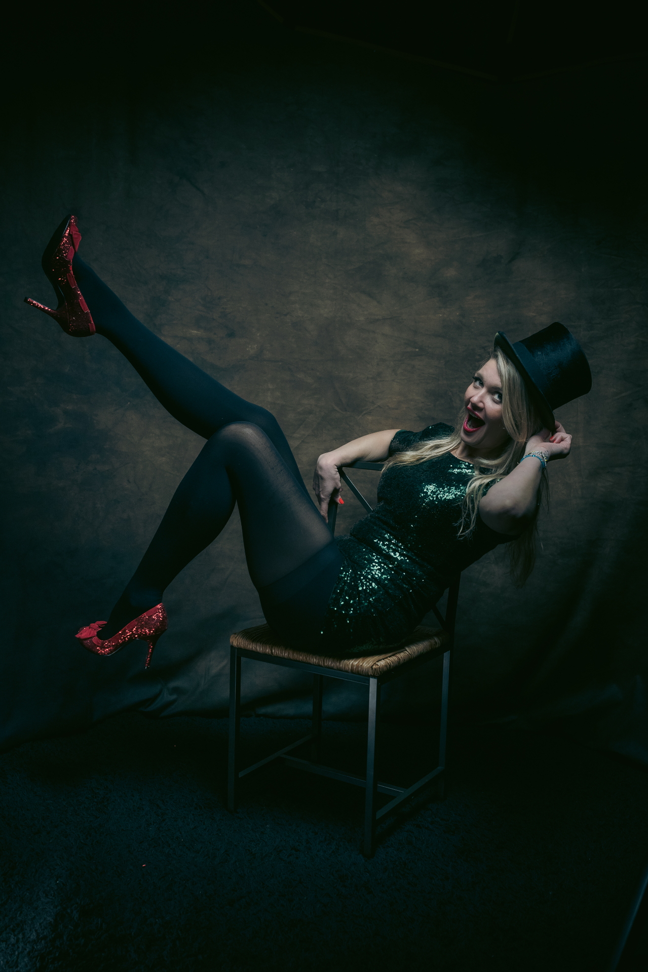 A playful seated portrait with red shoes and a top hat.